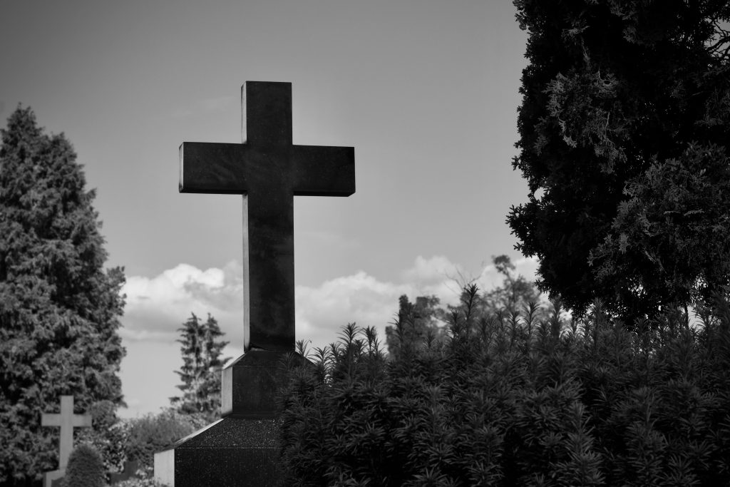 Serene black and white image of a cemetery cross amidst lush trees.