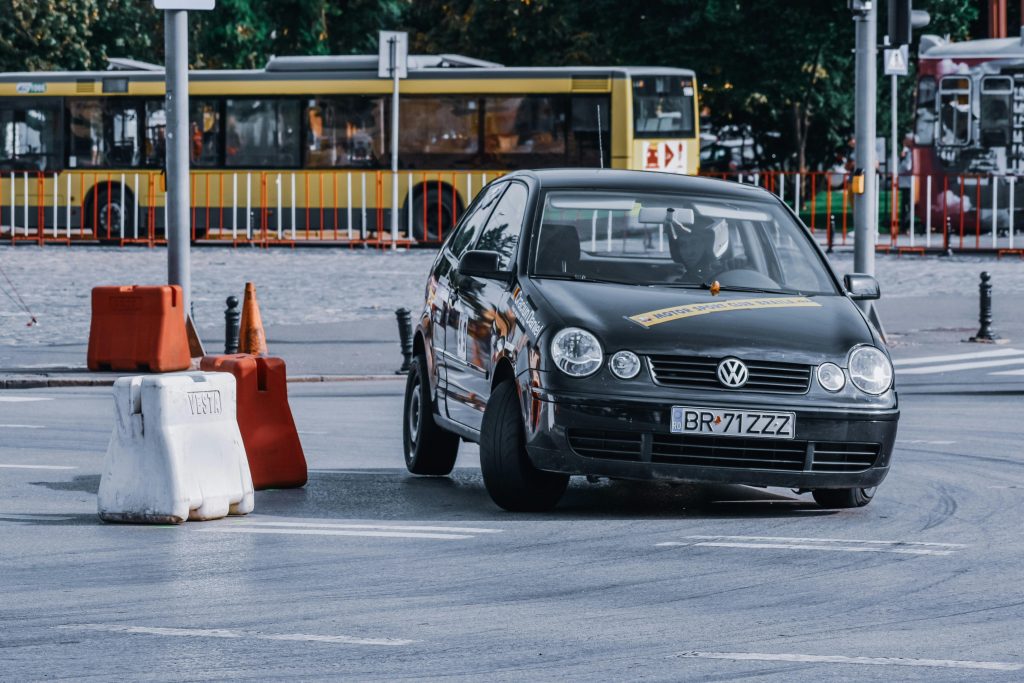 Black fast automobile driving through barriers on asphalt road against city district with bus route