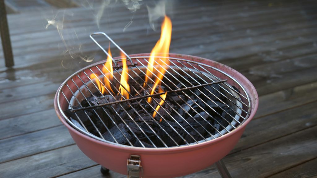 A charcoal grill with burning flames and smoke on a wooden deck, perfect for outdoor cooking.