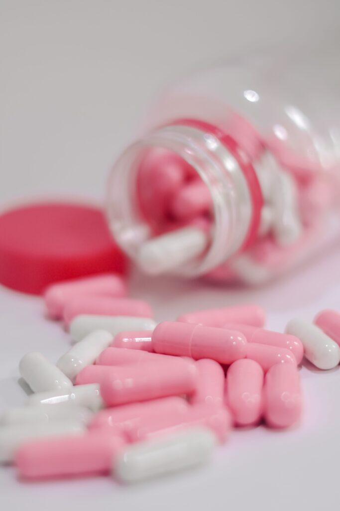 Zbliżenie różowych i białych kapsułek wylanych z butelki, przedstawiających farmaceutyki i leki